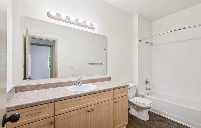 A bathroom with a sink, toilet, and mirror with lights at The Madison Apartments in Olympia, WA