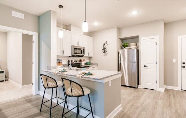 an open kitchen with a counter with three stools and a stainless steel refrigerator