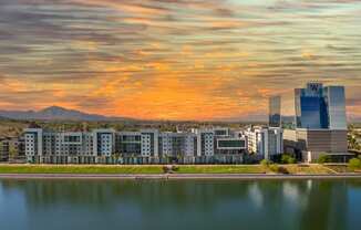 a cityscape with a lake in the foreground and a sunset in the background