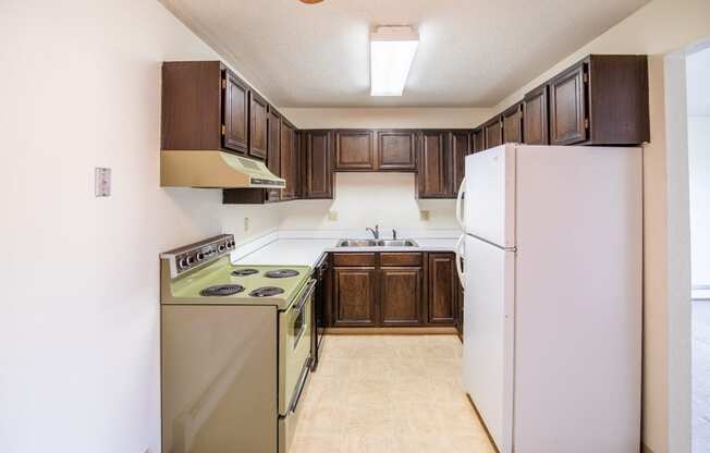 A kitchen with white appliances and brown cabinets and a refrigerator. Bismarck, ND Eastbrook Apartments .