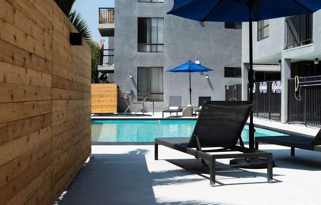 a pool with two lounge chairs and umbrellas in front of a building