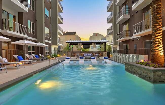 a swimming pool with lounge chairs and umbrellas in front of an apartment building