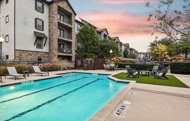 A swimming pool in front of apartment buildings at dusk.