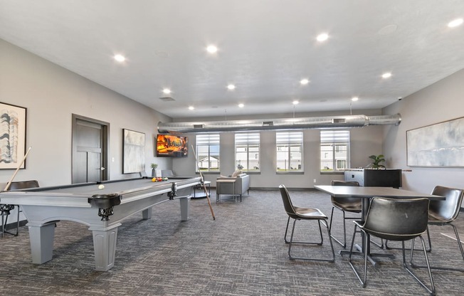 A room with a pool table, chairs, and a TV.
