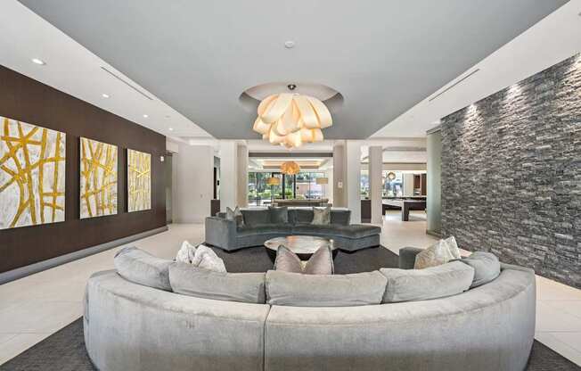 A modern living room with a large grey couch and a stone wall.