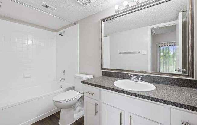 B1 white bathroom with a toilet, sink, vanity lights, and mirror at Jefferson Place Apartments in Irving, TX