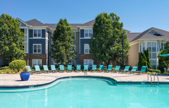 Chapel Hill, NC, Luxury Apartments with In-Unit Washers and Dryers - The Reserve at Meadowmont - Resort-Style Swimming Pool with Sundeck, Lounge Chairs, Surrounding Trees, and Apartment Buildings in the Background.