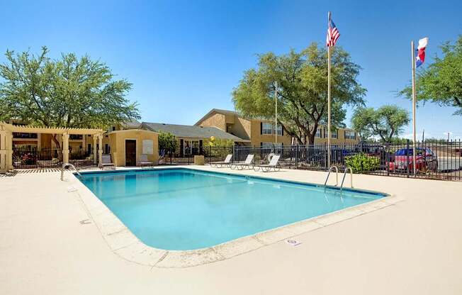 A refreshing outdoor swimming pool here at Avalon Springs with clear blue water, surrounding lounge chairs, and shaded pergola seating, enclosed by secure fencing and mature trees that create a relaxed, community-focused atmosphere.