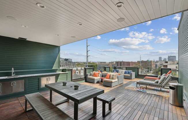 A wooden table and chairs are set up on a wooden deck with a city skyline in the background.