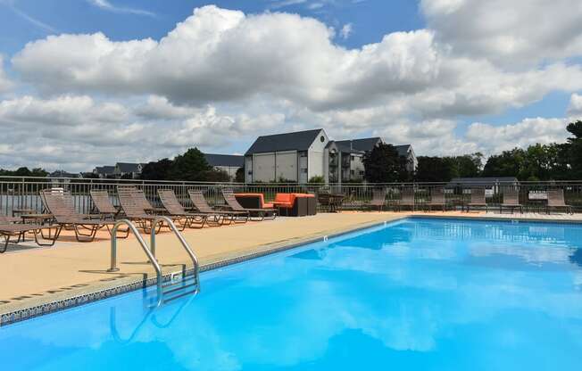 a swimming pool with chairs and a blue sky with clouds