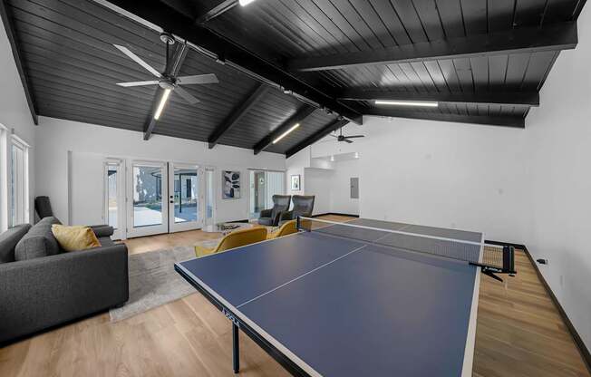 A ping pong table is in the middle of a room with a grey couch and a wooden floor.