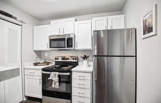 A kitchen with white cabinets and a stainless steel refrigerator.