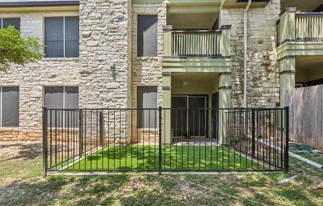 A black iron fence surrounds a green lawn in front of a stone building.