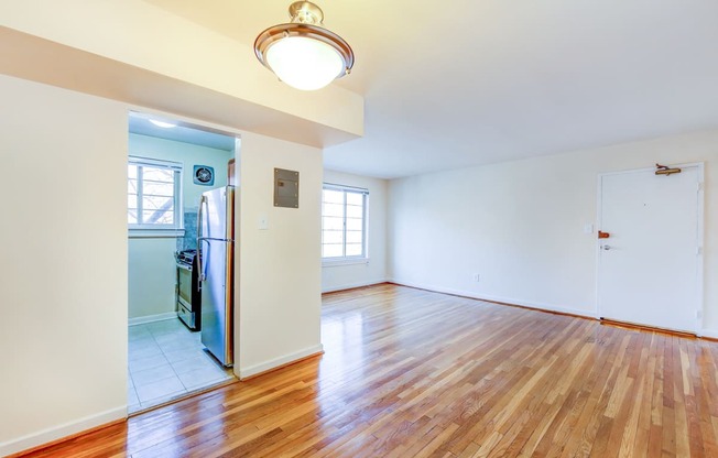 vacant living area with large windows, hard wood flooring and view of kitchen in cambridge square apartments in bethesda md