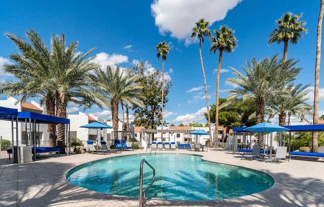 a swimming pool with blue umbrellas and palm trees in the background