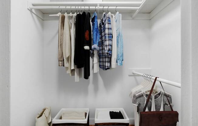 a closet with clothes hanging on a rack and two boxes on the floor