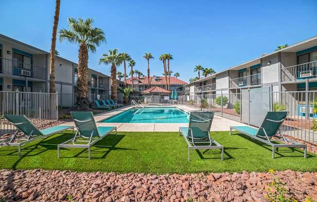 a pool with two lounge chairs and palm trees in front of an apartment building