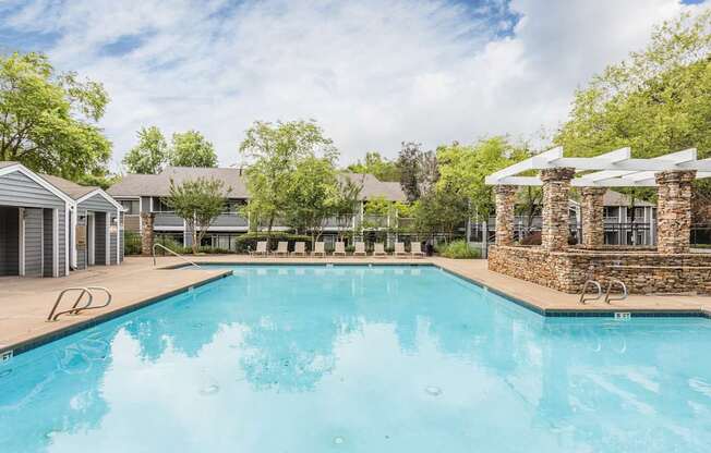 A large swimming pool surrounded by trees and a stone building.