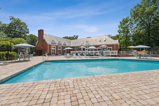 A large outdoor swimming pool with a brick patio and a house in the background.