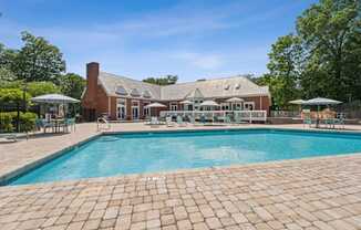 A large outdoor swimming pool with a brick patio and a house in the background.