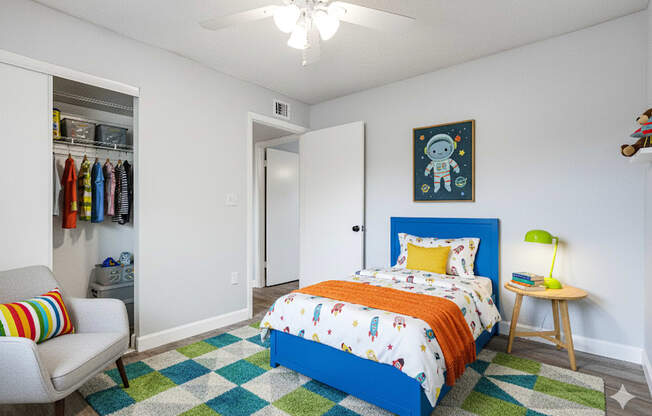 A bedroom with a blue bed and a grey chair.