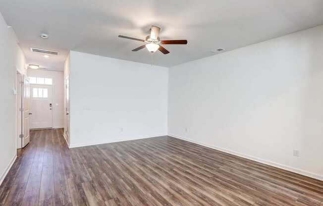 Four-BR Townhomes in North Charleston, SC - Highland Townhomes - Empty Living Room With White Walls, Wood-Style Flooring, and A Ceiling Fan