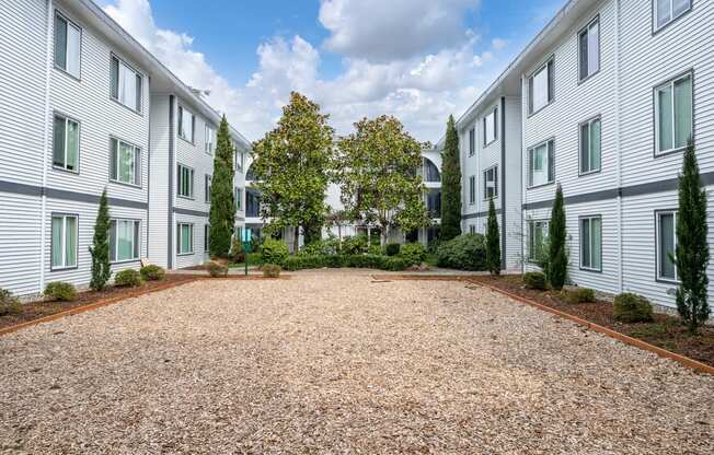 the courtyard of an apartment building with trees and gravel