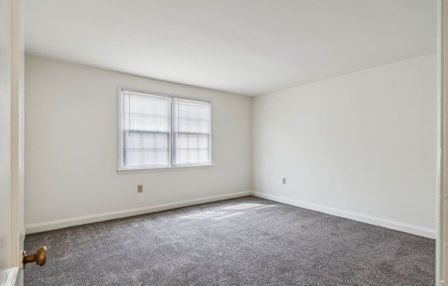 a bedroom with white walls and carpet and a window