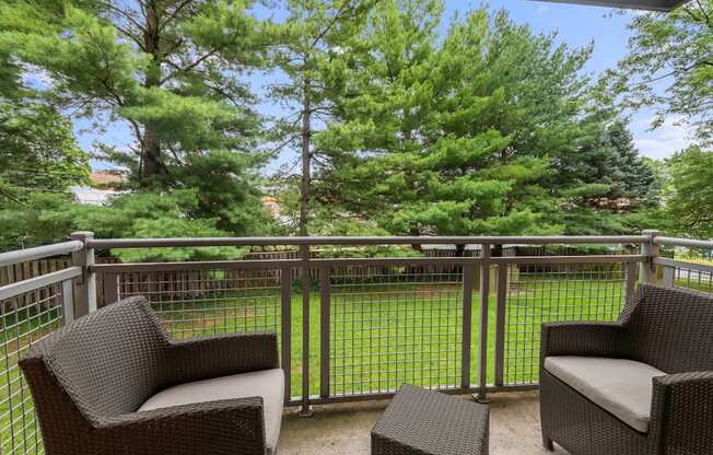 Two chairs and a table on a balcony with trees in the background.