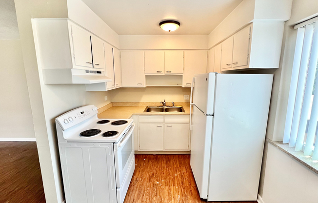 Charming kitchen with modern white cabinetry, efficient appliances, and warm wood-style flooring.