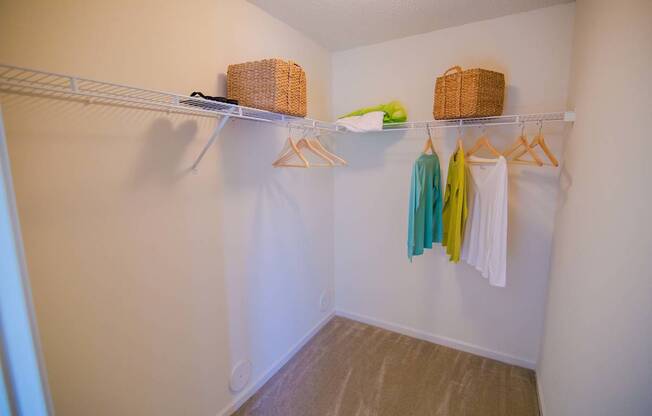 A white closet with clothes hanging and baskets on the shelf.