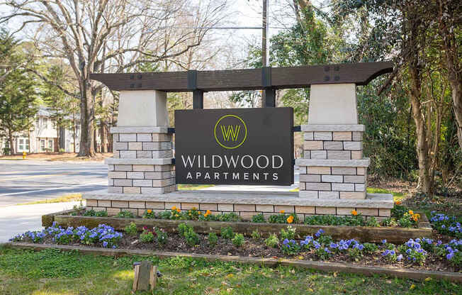 A sign for Wildwood Apartments is surrounded by flowers and greenery.