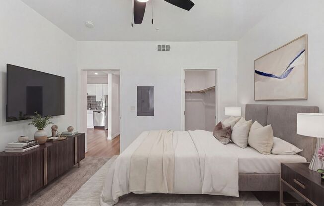 Elegant bedroom showcasing a plush bed with neutral-colored bedding, contemporary decor, and a wall-mounted television, opening into a sleek kitchen area.