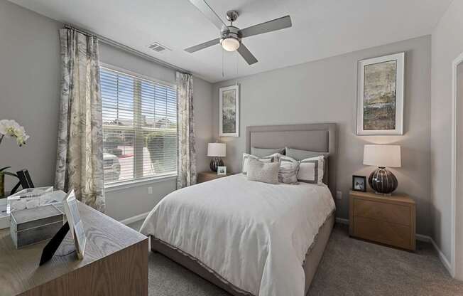 A bedroom with a large bed, a ceiling fan, and a window with curtains.