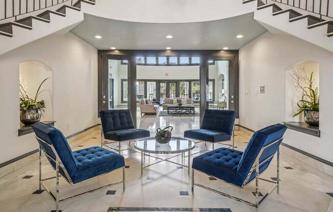 Four blue chairs are arranged around a glass table in a spacious room.