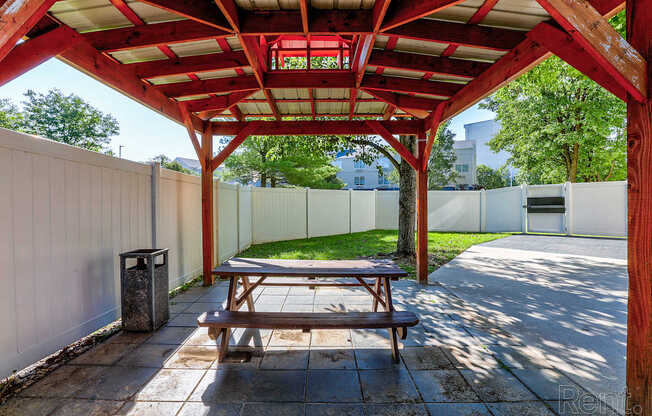 A wooden picnic table is under a red and white canopy.