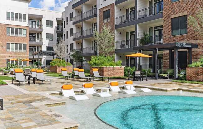 A pool surrounded by orange chairs and buildings in the background.