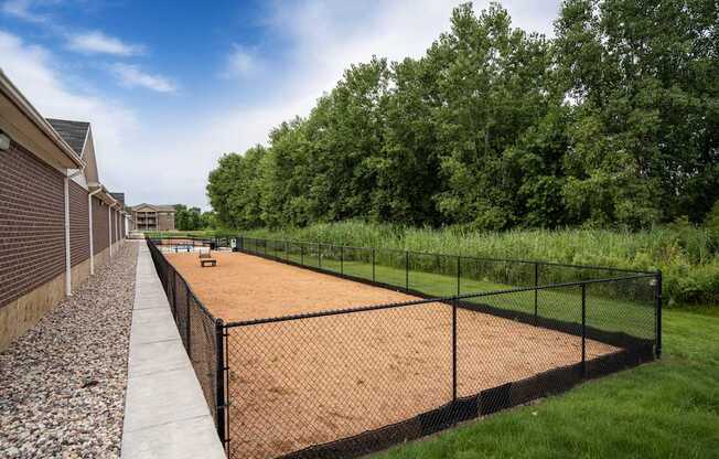 A tennis court is surrounded by a black fence and a gravel path.