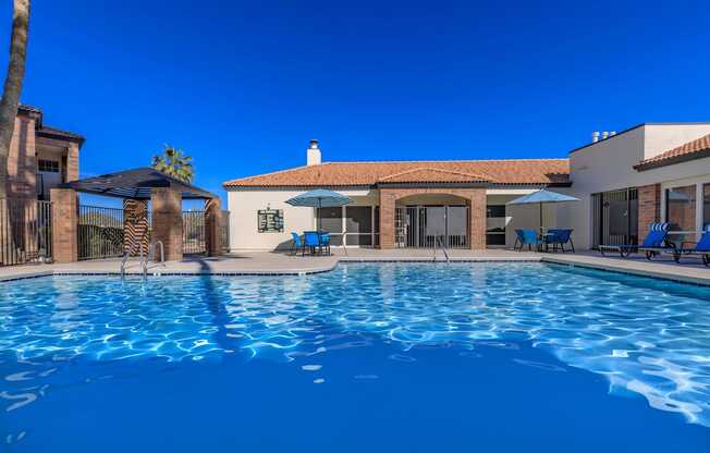 A swimming pool in front of a house with a blue sky.