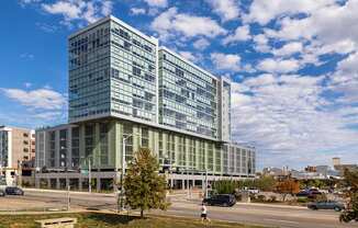 A large glass building with a green roof stands in front of a cloudy sky.