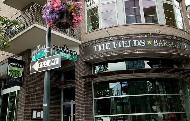A sign for The Fields Bar & Grill is displayed on a pole in front of a building.