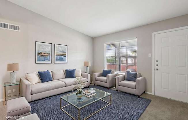 A living room with a glass coffee table and a couch with blue pillows.