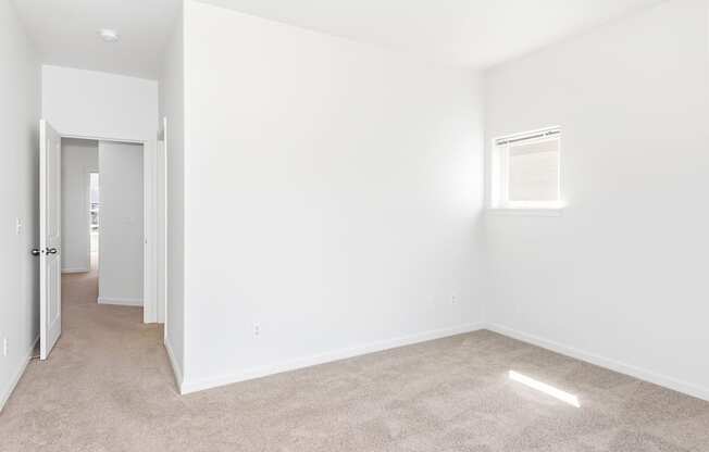 A spacious, empty room with a carpeted floor and a small window at The Landing Apartments and Townhomes, Oregon, 97045