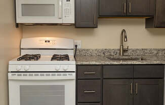 A white stove and microwave in a kitchen with dark brown cabinets.