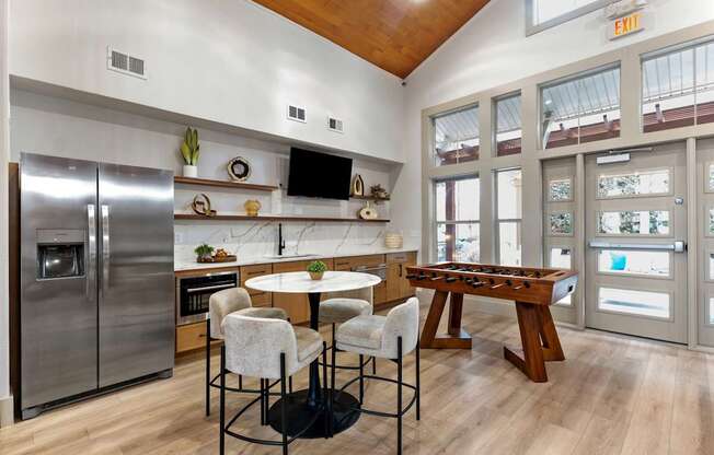 A kitchen with a refrigerator, a dining table, and chairs.