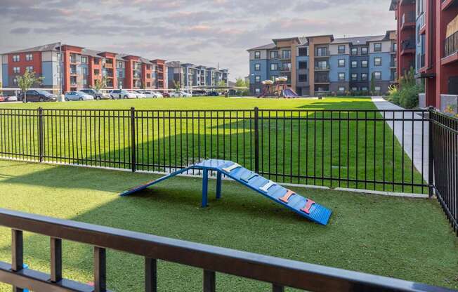 A playground with a blue slide in the foreground and apartment buildings in the background.