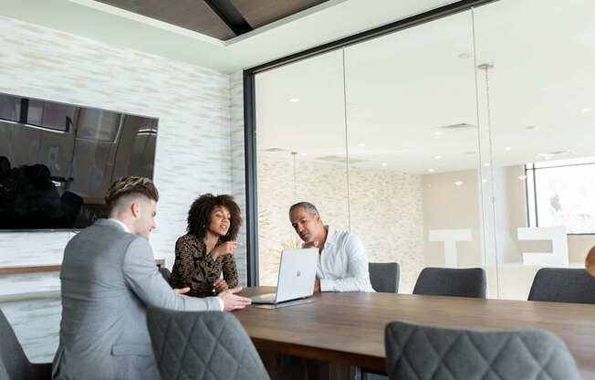 Three people are sitting around a table in a meeting room.