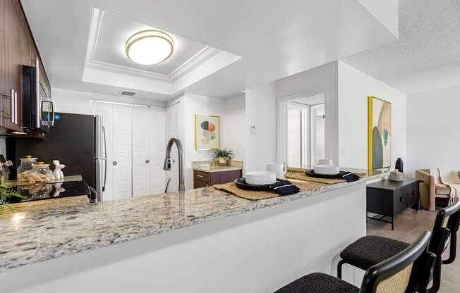 A modern kitchen with a marble countertop and black chairs.