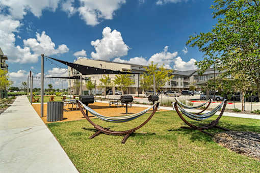 A park with a hammock and a building in the background.