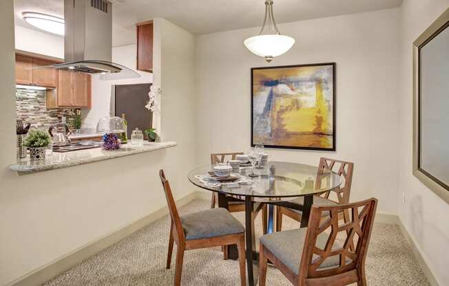 a dining area with a glass table and chairs and a kitchen in the background